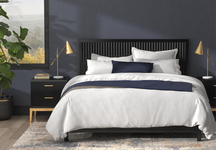 Image of a neatly made bed in a navy blue room with mostly white bedding and a few Midnight accents