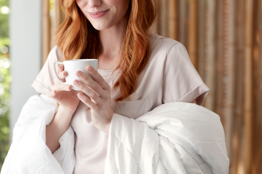 Image of a woman wrapped in a Duvet Insert hiding a coffee cup