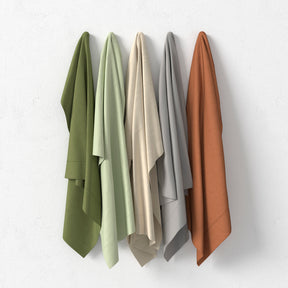 Image showcasing all five colors for the Recovery Viscose Sheet Set hanging on a white wall. The colors include (from left to right): Moss, Sage, Ivory, Dove Gray, Clay
