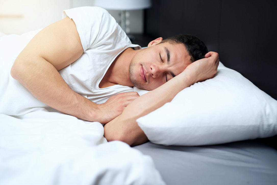 Image of a man asleep on his side with all-white bedding