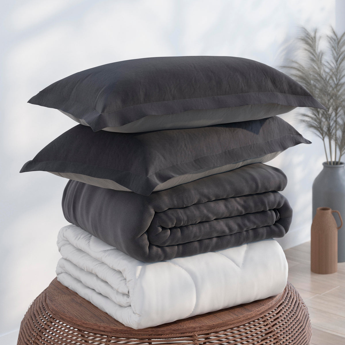 Image of the Dove Gray/Shadow Soft Touch Bundle on top of a brown table. The bedding shown includes (from top to bottom): 2 Dove Gray/Shadow Pillow Shams with the Shadow side facing up, a neatly folded Dove Gray/Shadow Soft Touch Duvet Cover with the Shadow side showing, and a neatly folded Soft Touch Duvet Insert 