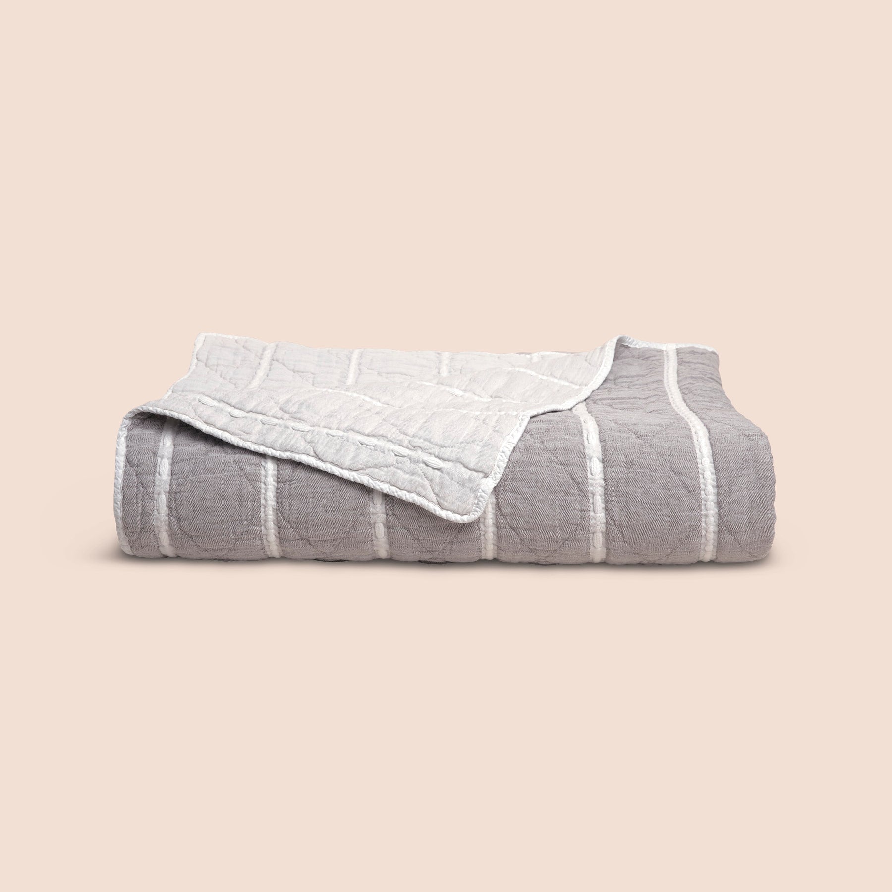 Image of a neatly folded gray and white striped Heritage Quilt with a corner folded over to reveal the reversible lighter side on a light pink background