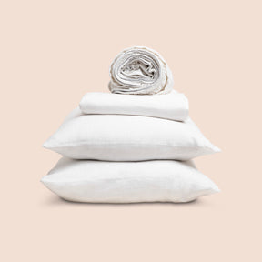 Image showcasing entire White Blended Linen Sheet Set on a light pink background. Set features a rolled-up fitted sheet on top, a neatly folded flat sheet, and two stacked pillowcases. 