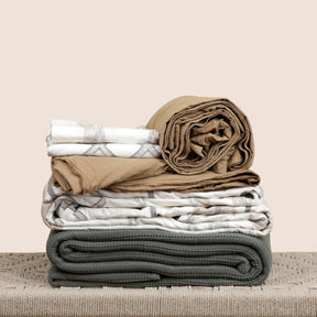 Image of the entire Sonoran Bundle on a tan bench with a light pink background. The bundle featured showcases from top to bottom: 2 Sonoran Pillow Shams, Ochre Garment Washed Percale Sheets, a Sonoran Duvet Cover, and an Agave Ridgeback Coverlet.