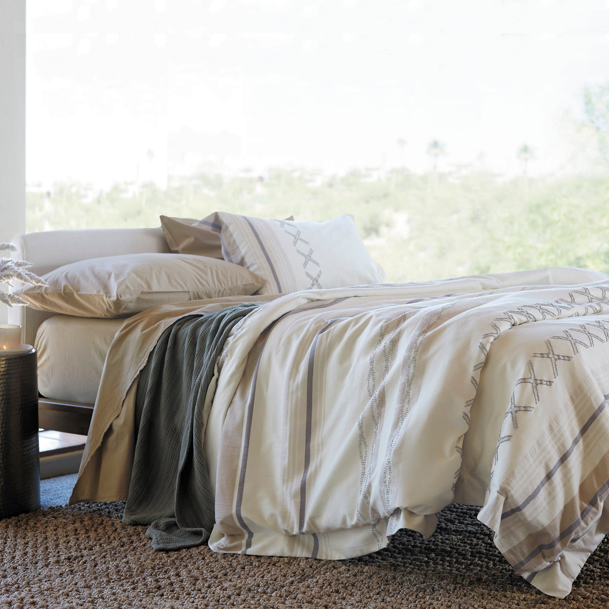 Image of a made bed with a large window behind it. The bed showcases Ochre Garment Washed Percale Sheets, an Agave Ridgeback Coverlet, and a Sonoran Duvet Cover.
