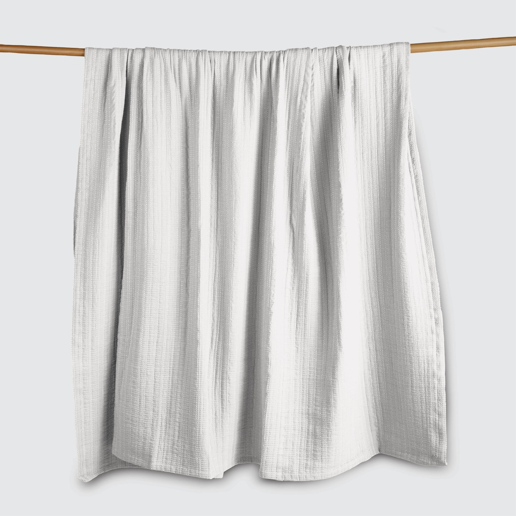 Image of a Bright White Everyday Cotton Coverlet hanging and draped over a wooden rod on a white background