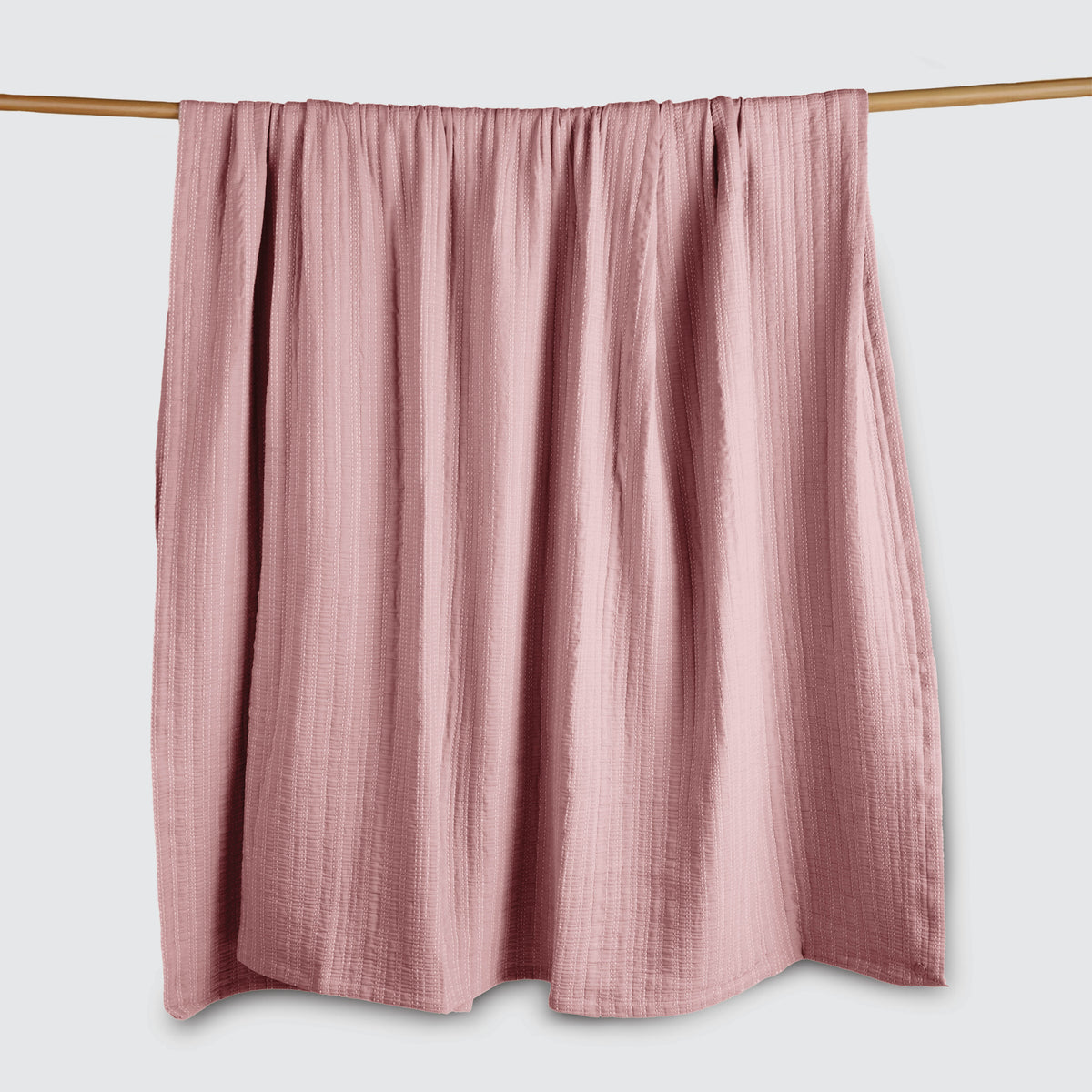 Image of an Ash Rose Everyday Cotton Coverlet hanging and draped over a wooden rod on a white background