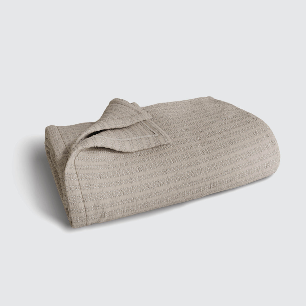 Image of an Oatmeal Everyday Cotton Coverlet folded up on a white background