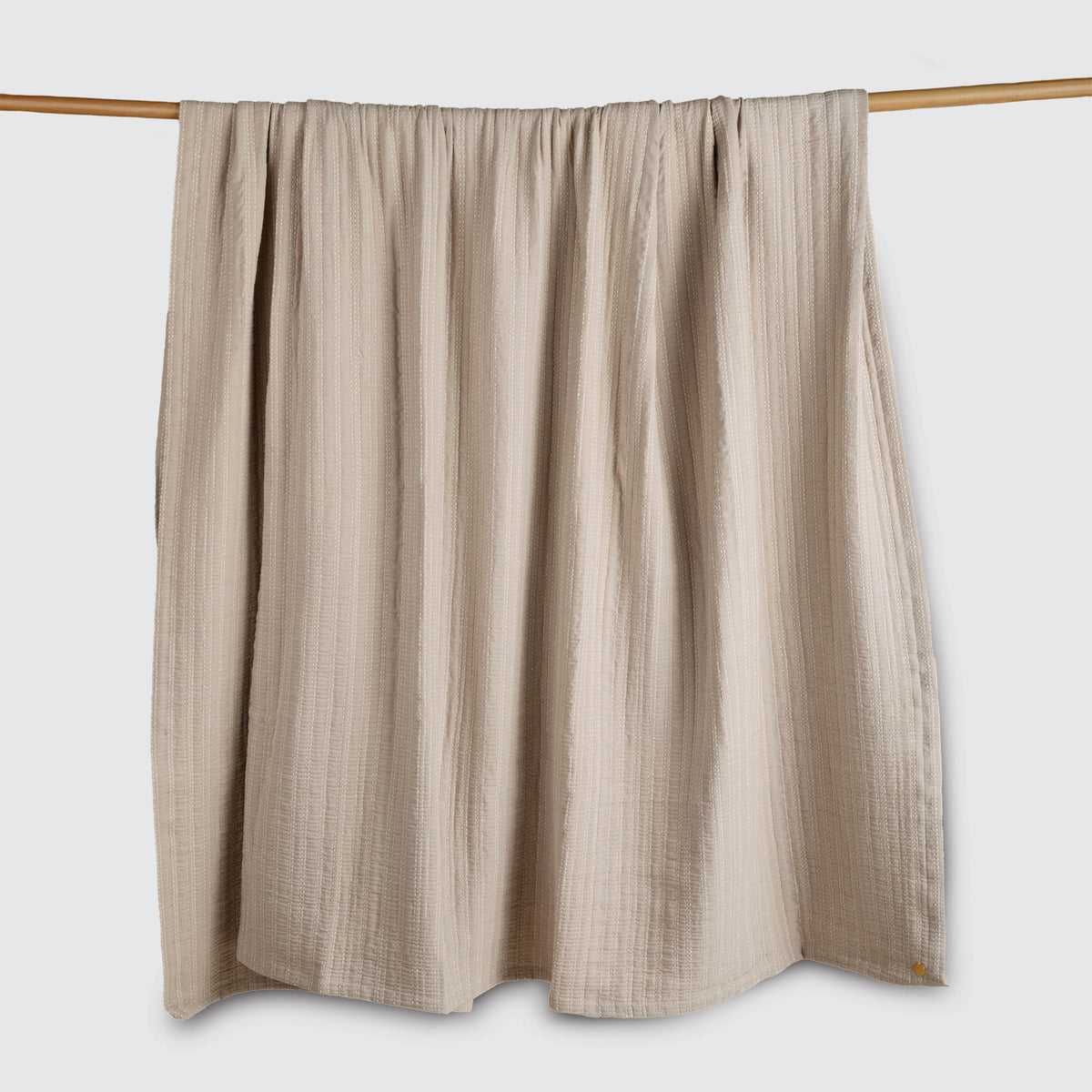 Image of an Oatmeal Everyday Cotton Coverlet hanging and draped over a wooden rod on a white background