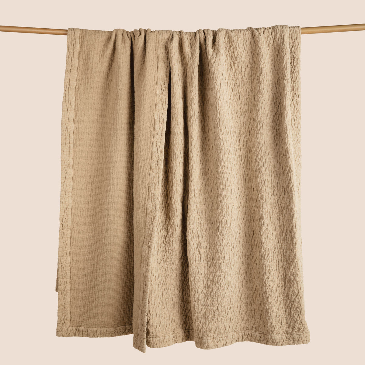 Image of an Ochre Wave Coverlet hanging and draped over a wooden rod on a light pink background