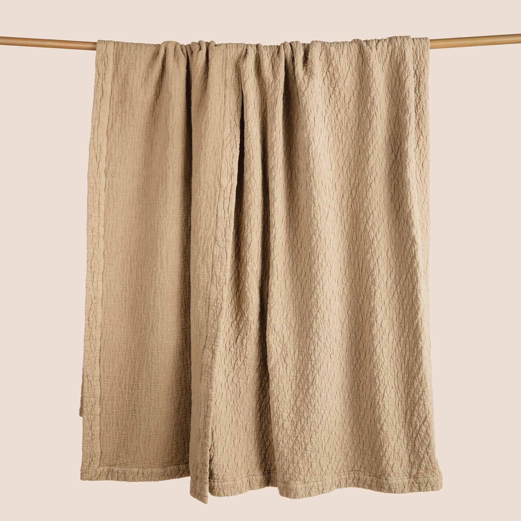 Image of an Ochre Wave Coverlet hanging and draped over a wooden rod on a light pink background