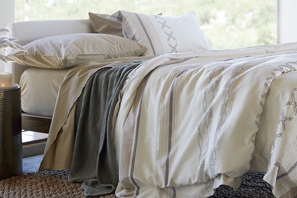 Image of a made bed with tan-colored sheets, an Agave Coverlet, and a Sonoran Duvet Cover and Pillow Sham