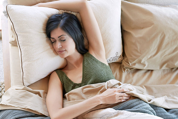 Image of a woman in a green tank top asleep in bed with her head resting on a Perfect Kapok Pillow and her arm draped over her head