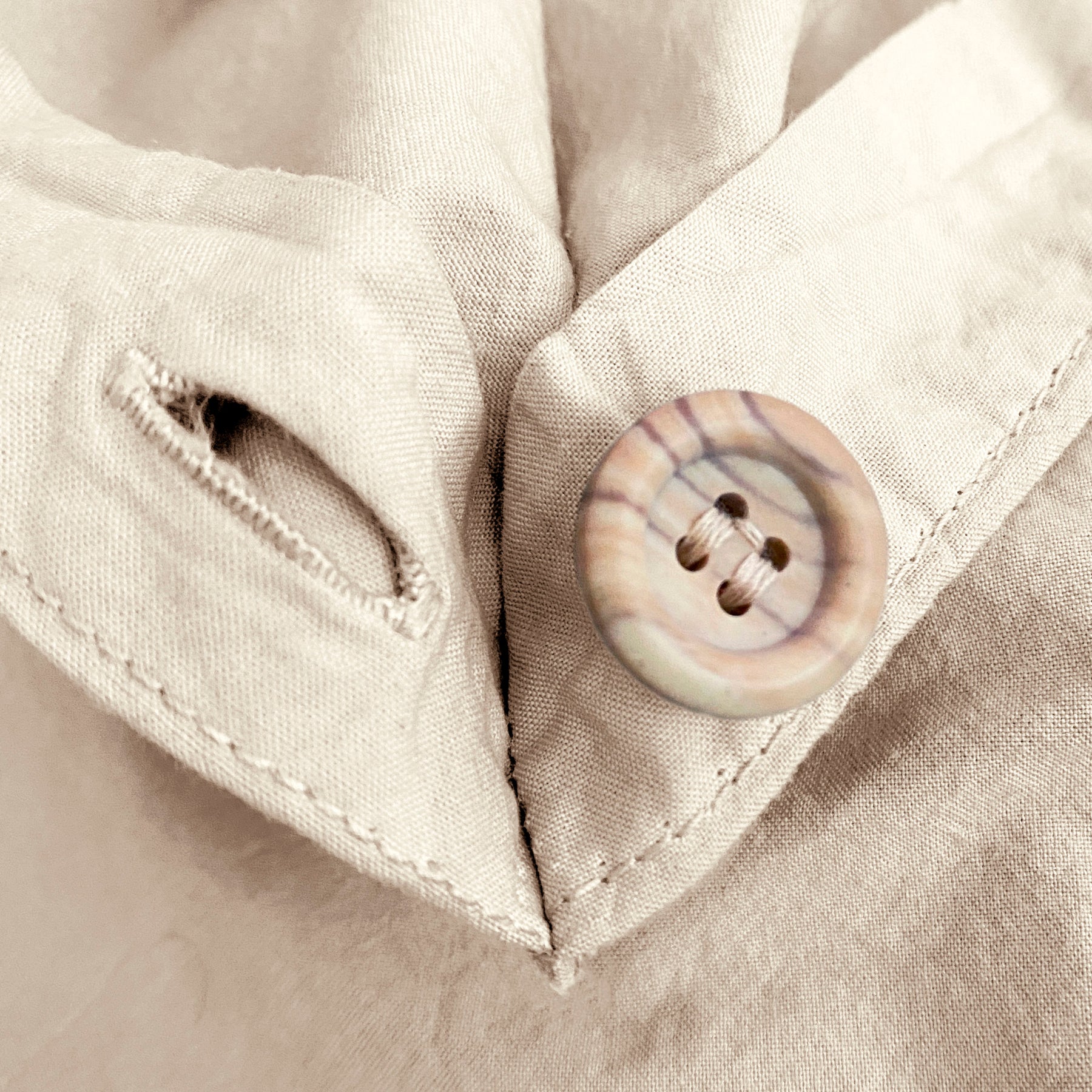 Close-up image of the button and button hole on the corner of an Ecru Garment Washed Percale Duvet Cover. 