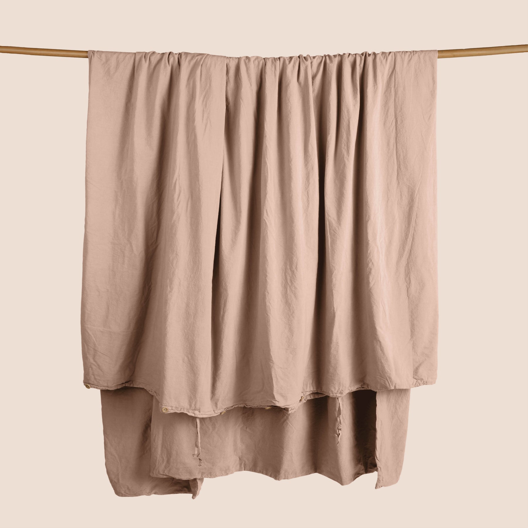 Image of a Pink Sandstone Garment Washed Percale Duvet Cover hanging and draped over a wooden rod on a light pink background