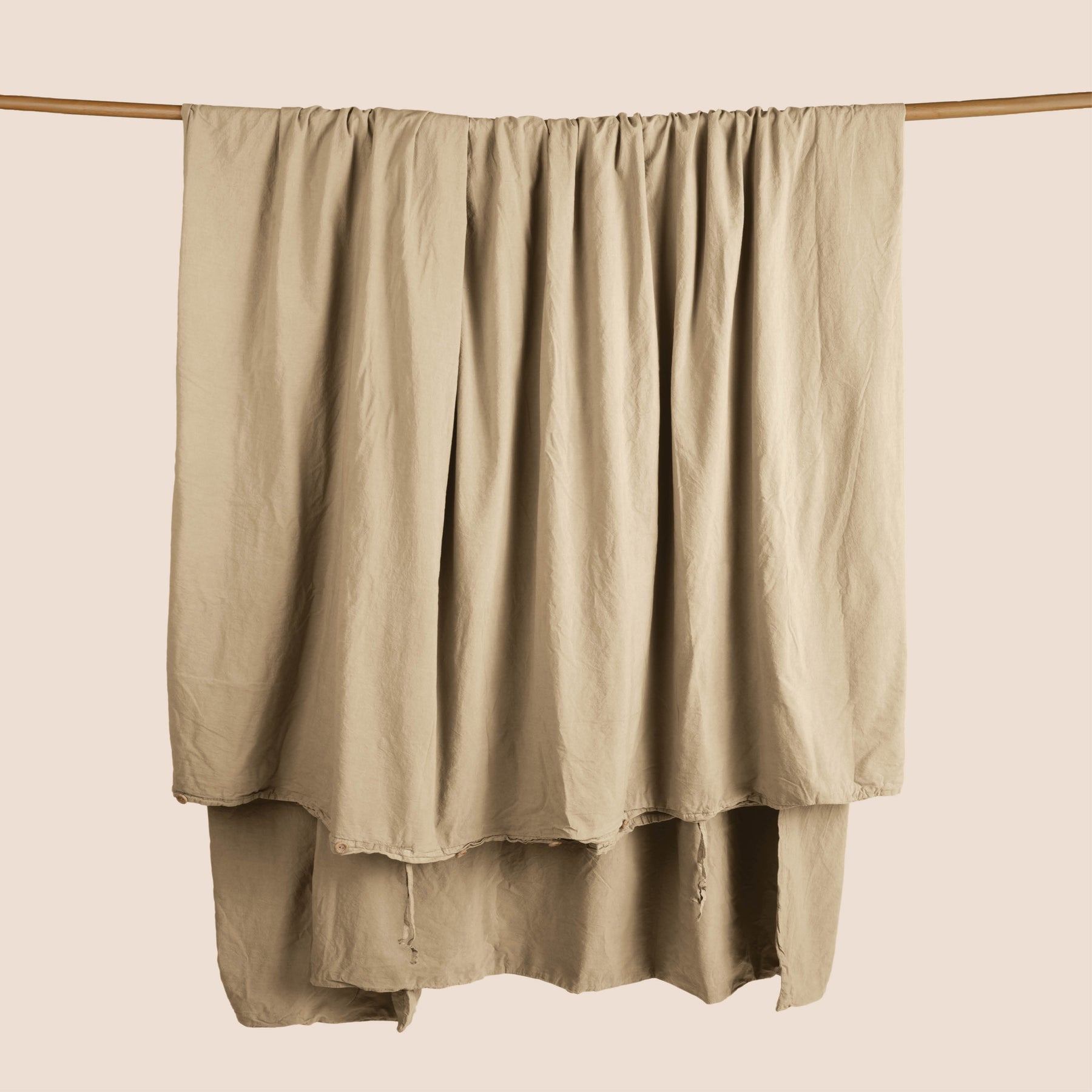 Image of an Ochre Garment Washed Percale Duvet Cover hanging and draped over a wooden rod on a light pink background