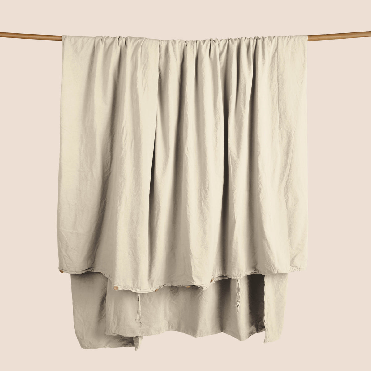 Image of an Ecru Garment Washed Percale Duvet Cover hanging and draped over a wooden rod on a light pink background