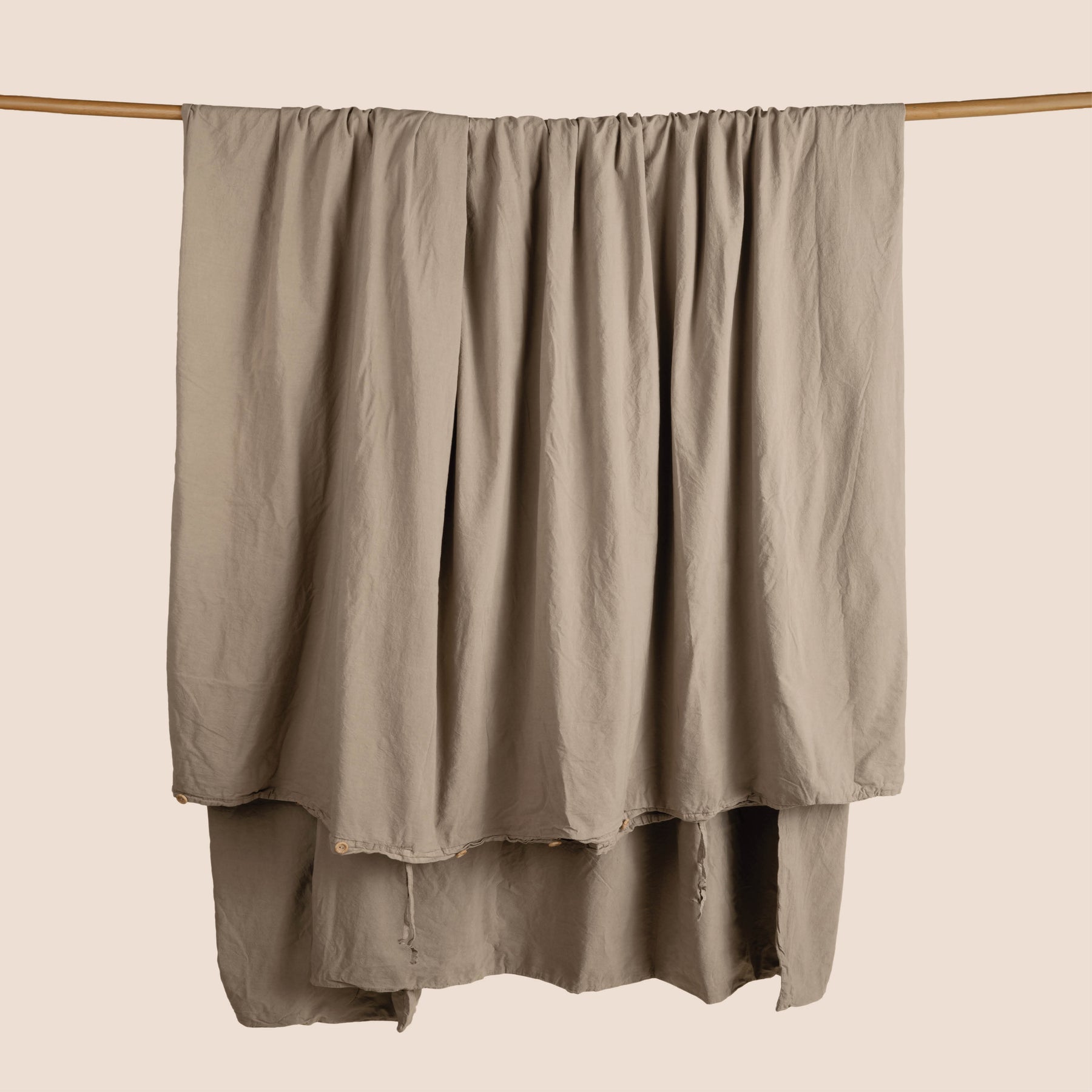 Image of a Desert Garment Washed Percale Duvet Cover hanging and draped over a wooden rod on a light pink background
