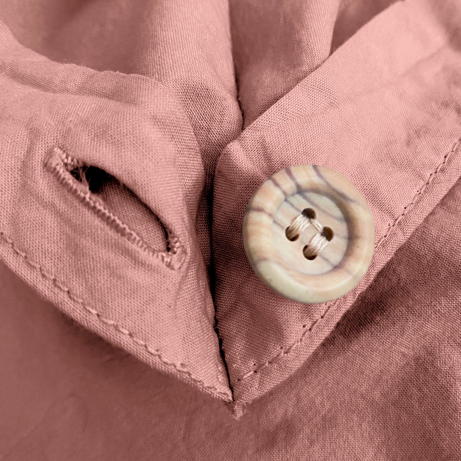Close-up image of the button and button hole on the corner of a Pink Sandstone Garment Washed Percale Duvet Cover.