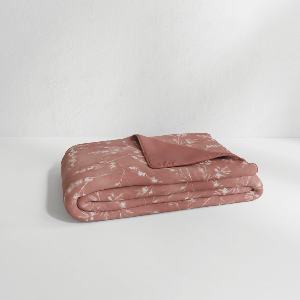Image of the Floral Ash Rose Duvet Cover + Cooling neatly folded with the floral side facing up and the back right corner folded over to show the reversible plain Ash Rose side