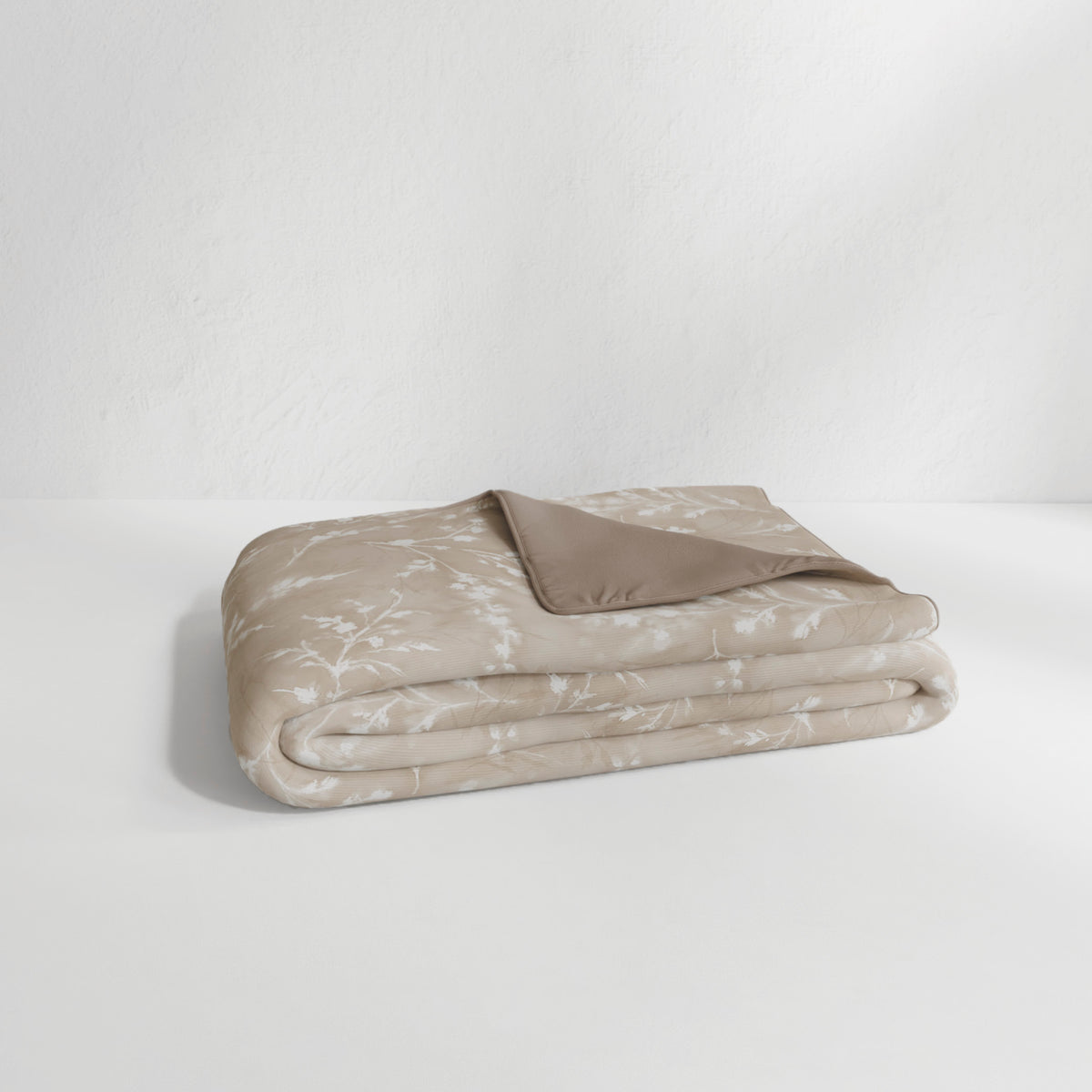 Image of the Floral Oatmeal Duvet Cover + Cooling neatly folded with the floral side facing up and the back right corner folded over to show the reversible plain Oatmeal side