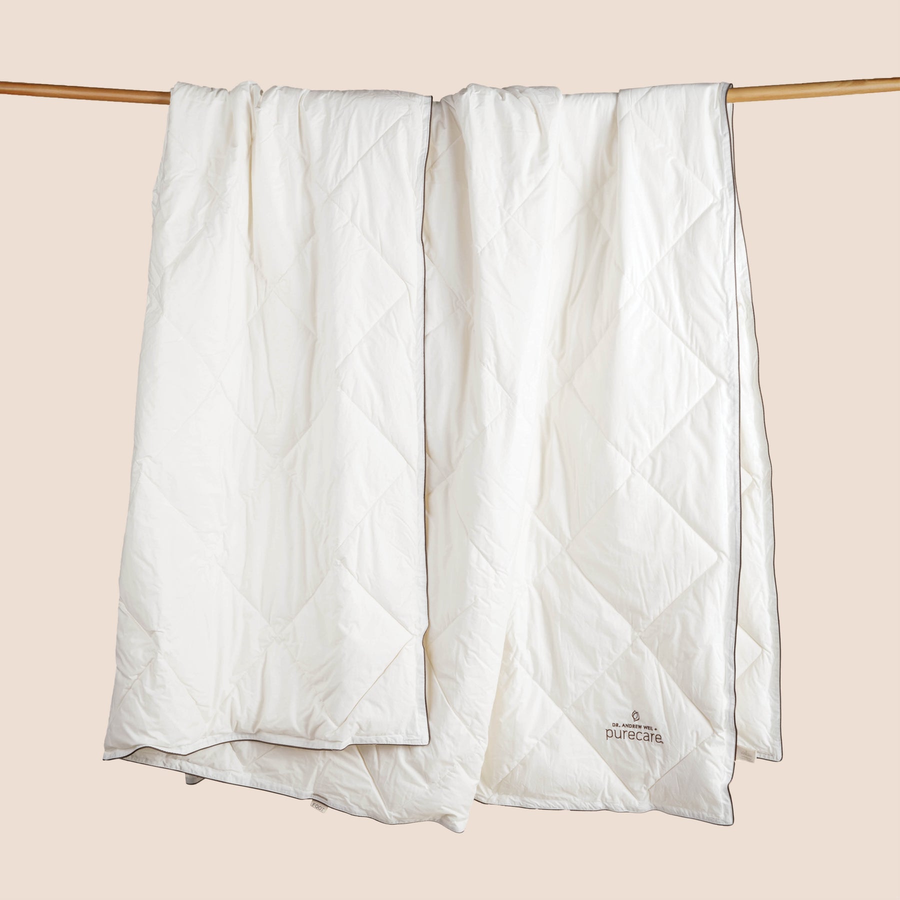 Image of an off-white All Seasons Wool Duvet Insert hanging and draped over a wooden rod on a light pink background