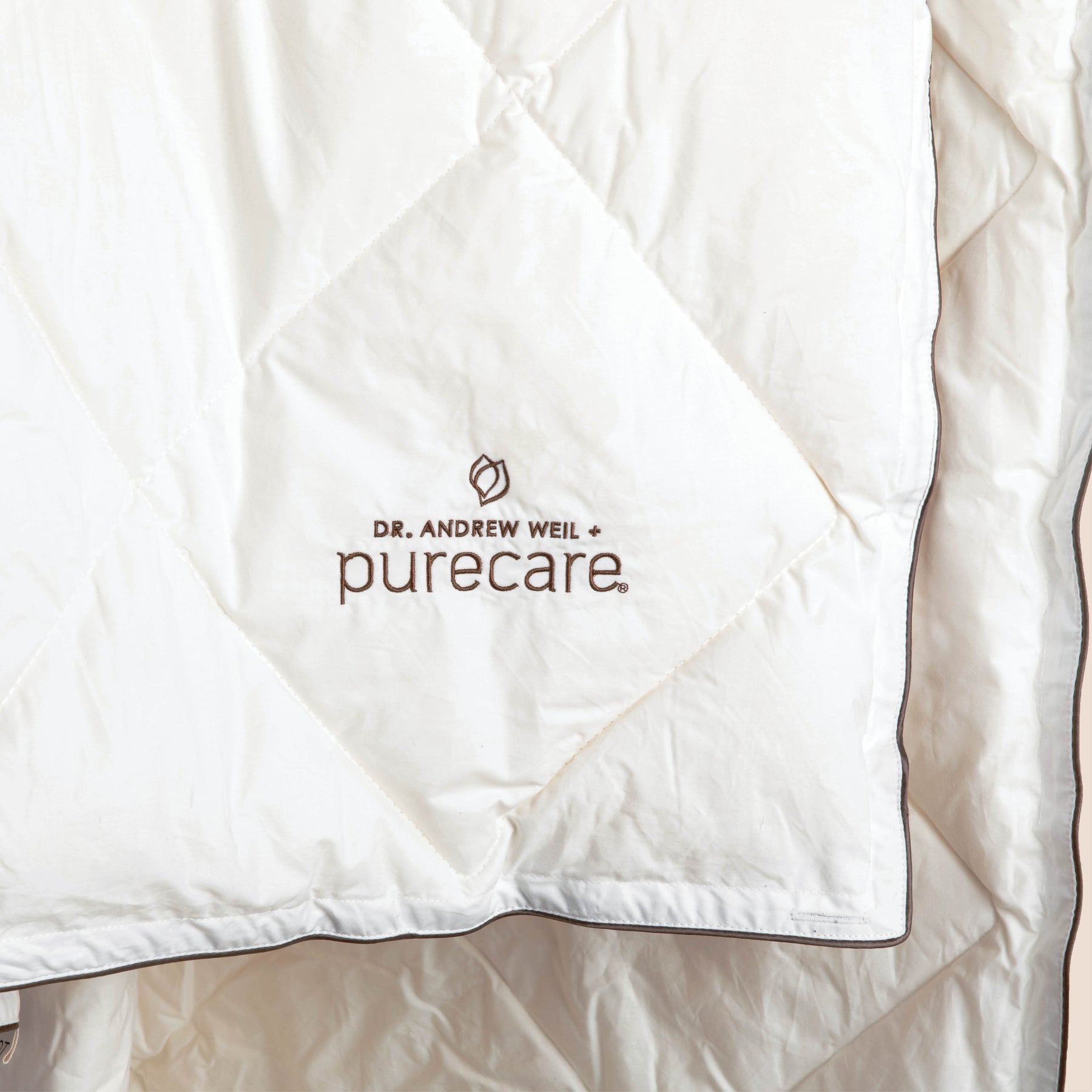 Close-up image of the Dr. Andrew Weil + Purecare logo sewn in brown onto the corner of the All Seasons Wool Duvet Insert