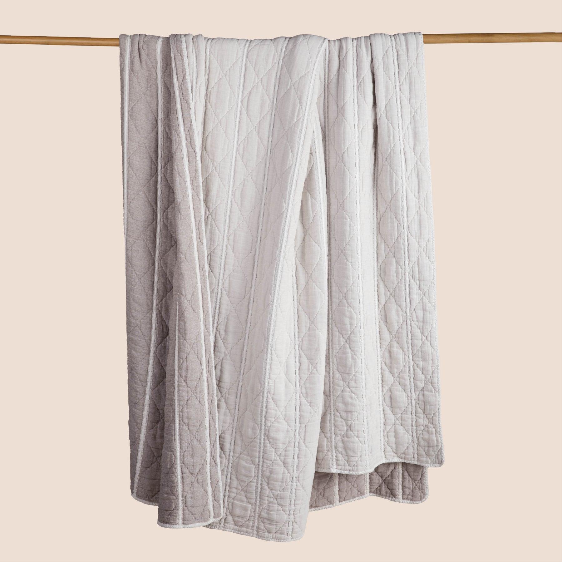 Image of the reversed all-white side of the Heritage Quilt hanging and draped over a wooden rod on a light pink background
