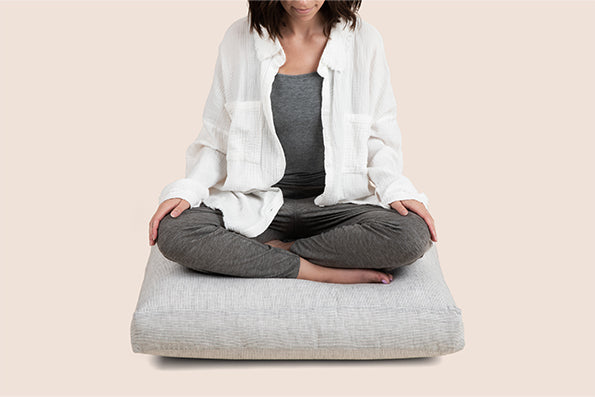 Image of a woman sitting on a meditation cushion with a gray cover on it