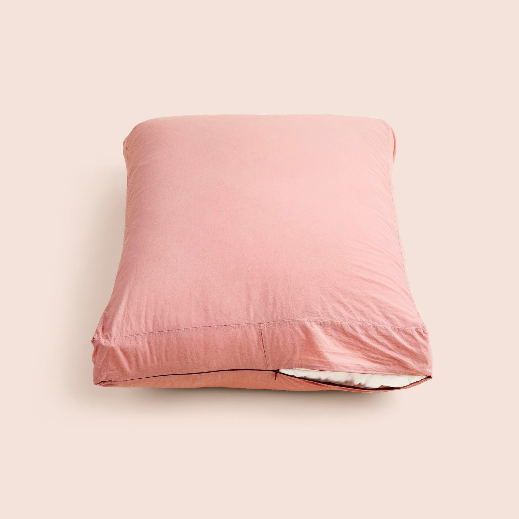 Image of Pink Sandstone Garment Washed Percale Meditation Cushion Cover showcasing a slightly opened zipper with a meditation cushion inside on a light pink background