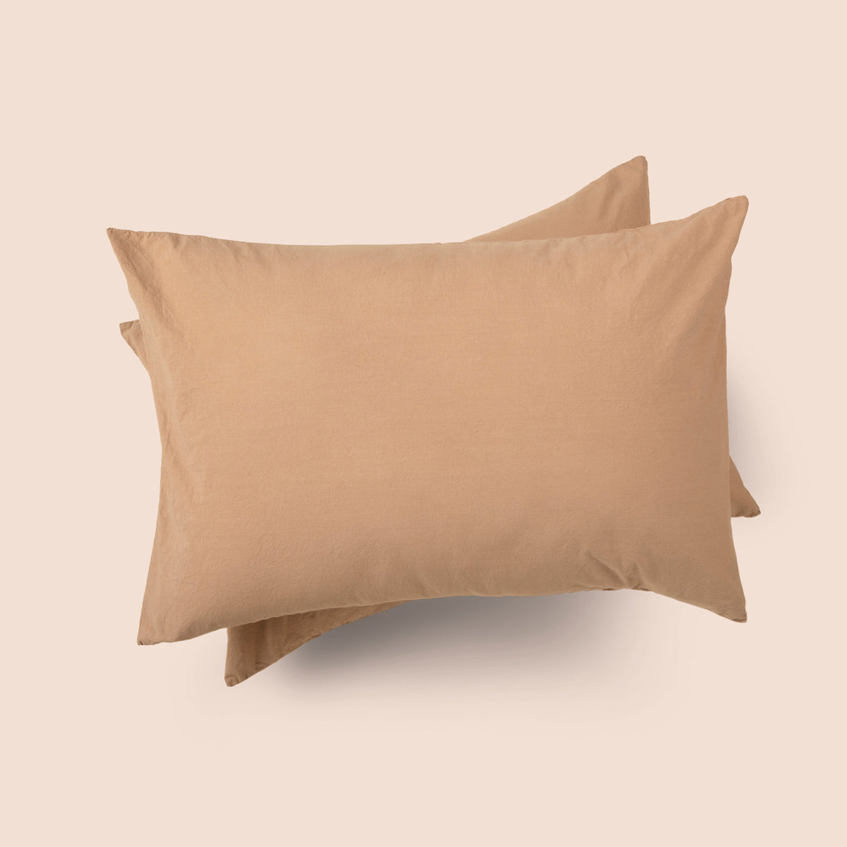 Image of the top of the Ochre Garment Washed Percale Pillow Sham on two pillows stacked on top of one another with a light pink background
