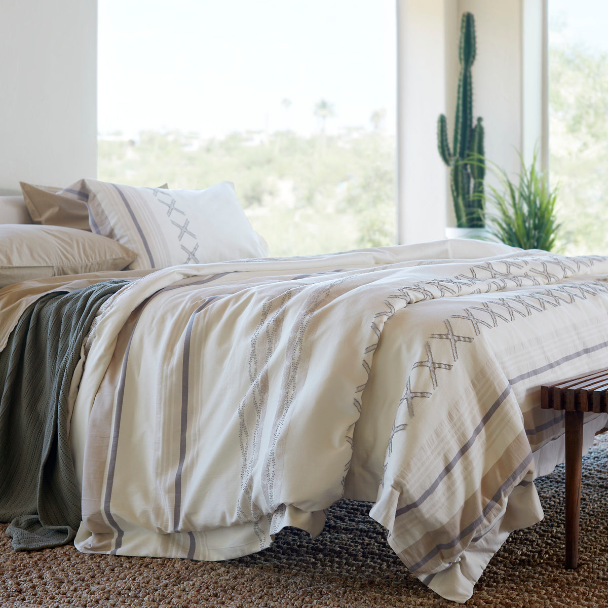 Image of a made bed with a large window behind it. The bed showcases Ochre Garment Washed Percale Sheets, an Agave Ridgeback Coverlet, and a Sonoran Duvet Cover.