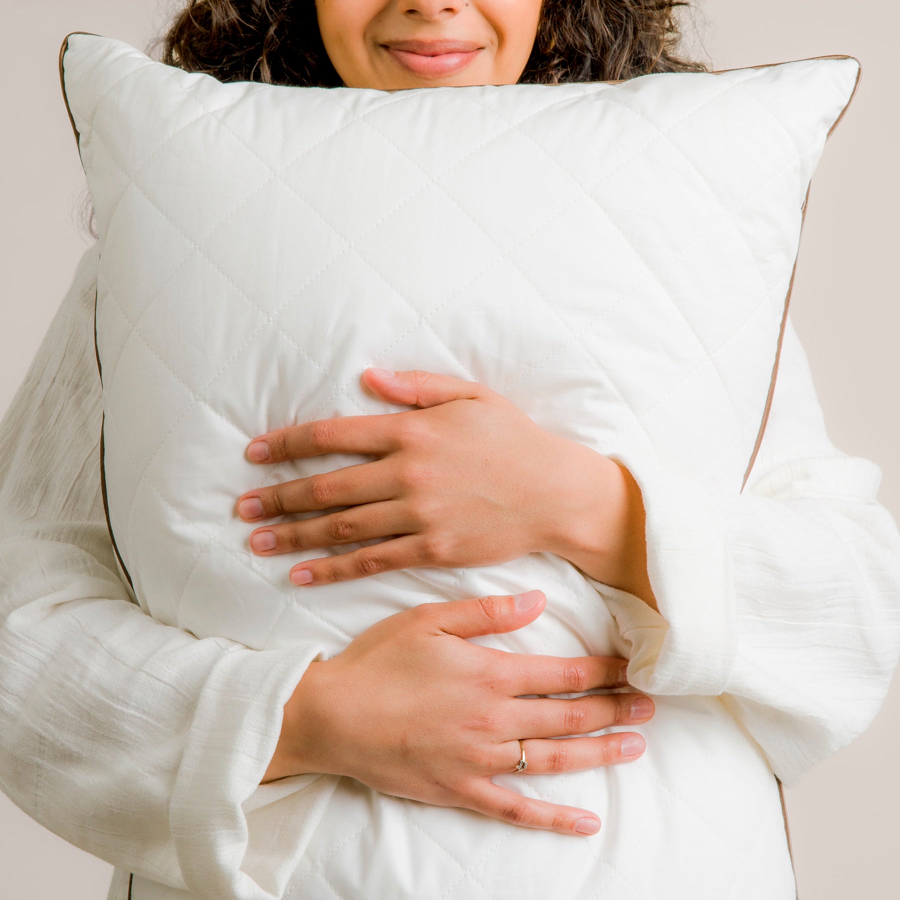 Image of smiling woman in white robe hugging the All Seasons Wool Pillow 