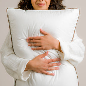 Image of smiling woman in white robe hugging the Chambered Down Pillow 