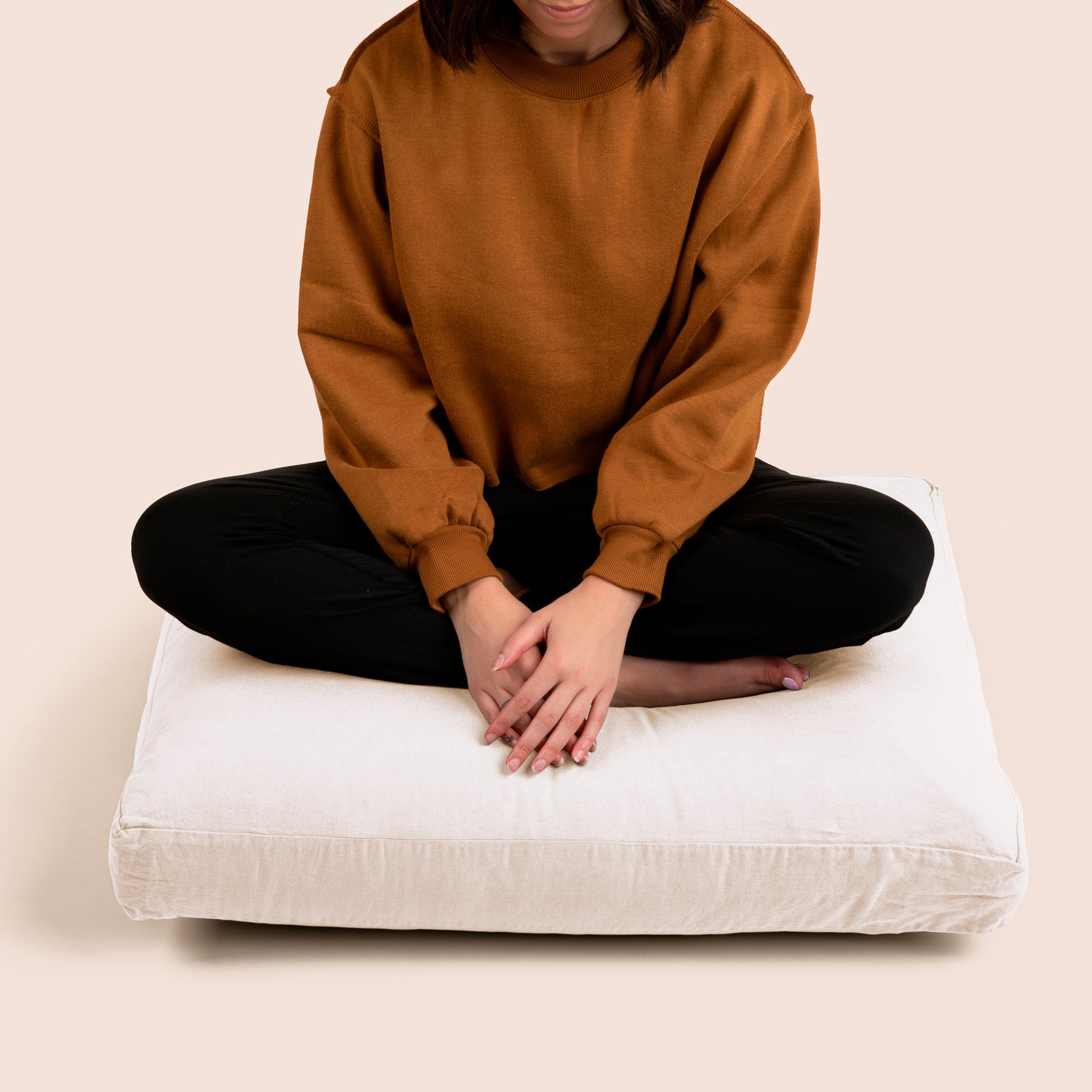 Image of a woman sitting cross-legged on the Meditation Cushion with a light pink background