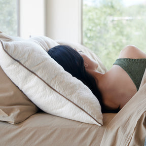 Image of a woman asleep in bed with her back towards the camera and her head resting on a Perfect Kapok Pillow
