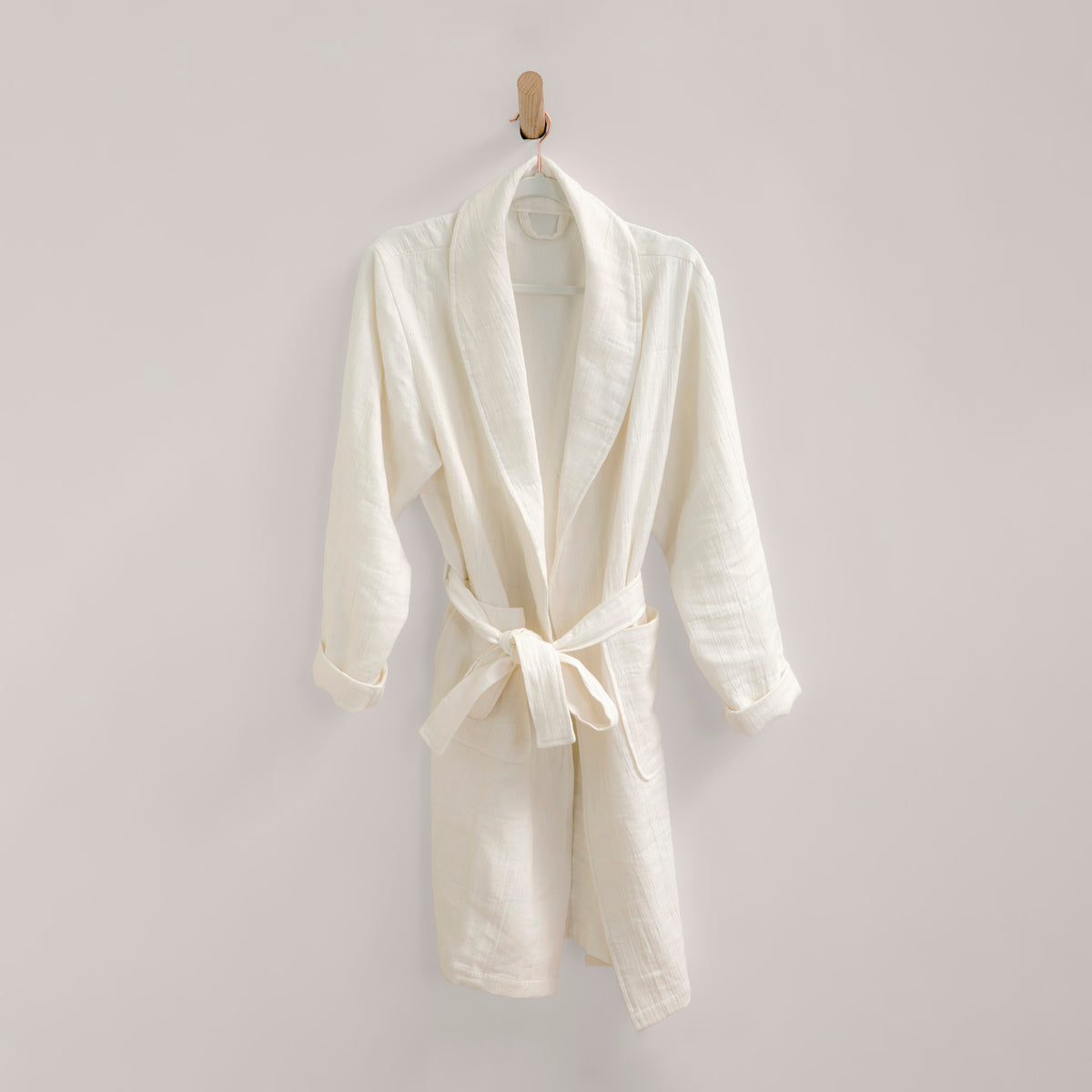 Image of white Featherweight Robe, tied and neatly hanging from a wooden peg on an off-white wall