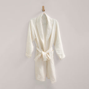 Image of white Featherweight Robe, tied and neatly hanging from a wooden peg on an off-white wall