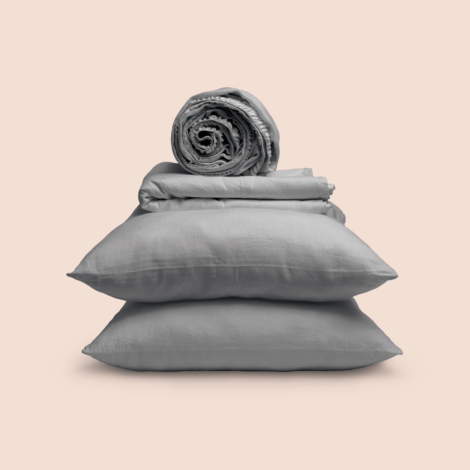 Image showcasing entire Stone Gray Blended Linen Sheet Set on a light pink background. Set features a rolled-up fitted sheet on top, a neatly folded flat sheet, and two stacked pillowcases.