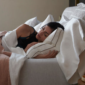 Image of a woman peacefully asleep in bed with a white sheet and pink coverlet covering her from the shoulders down