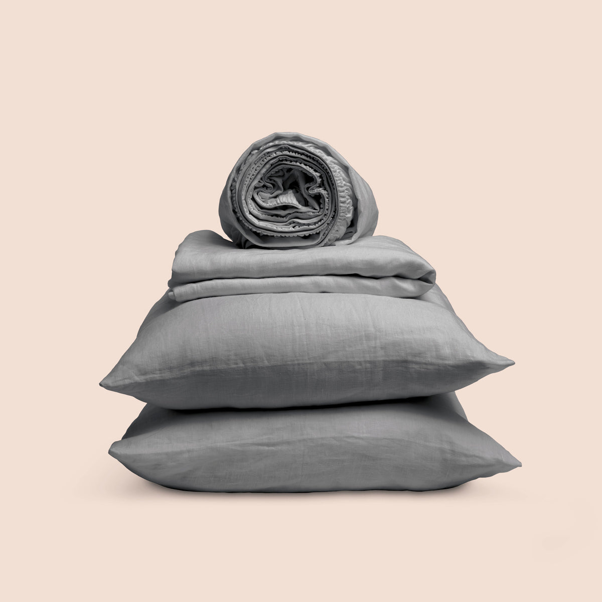 Image showcasing entire Stone Gray Relaxed Hemp Sheet Set on a light pink background. Set features a rolled-up fitted sheet on top, a neatly folded flat sheet, and two stacked pillowcases. 
