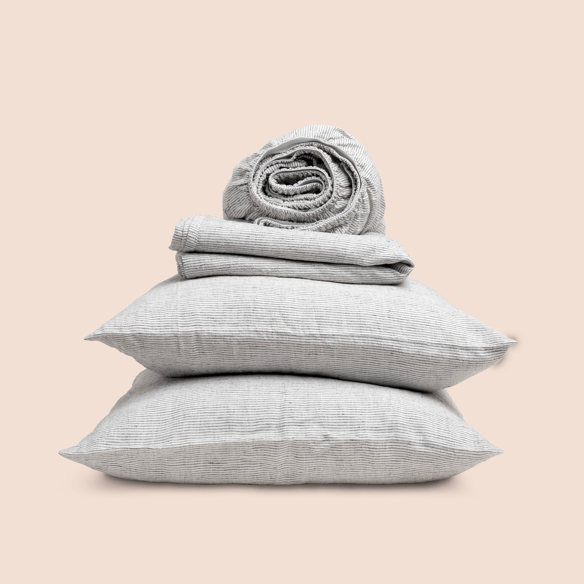 Image showcasing entire Pinstripe Relaxed Hemp Sheet Set on a light pink background. Set features a rolled-up fitted sheet on top, a neatly folded flat sheet, and two stacked pillowcases. 