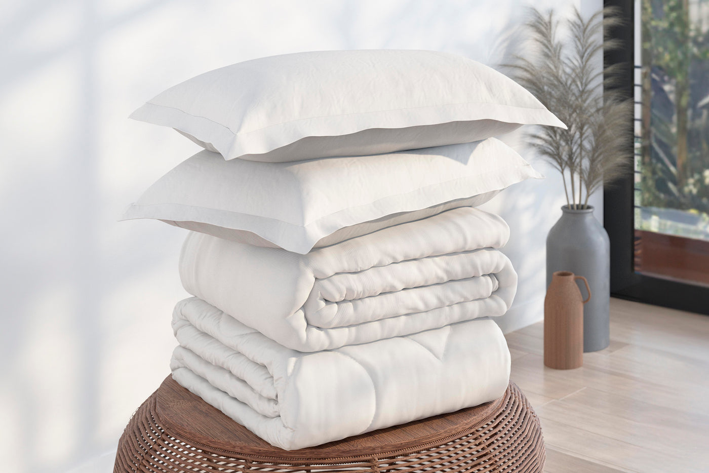 Image of a pile of bedding on top of a brown table. The bedding shown includes (from top to bottom): 2 White Pillow Shams, a neatly folded White Duvet Cover + Cooling, and a neatly folded Cooling Duvet Insert