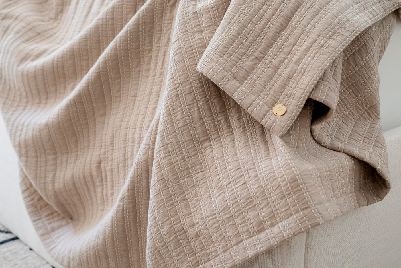 Image of the Oatmeal Everyday Cotton Coverlet on the side of a white couch