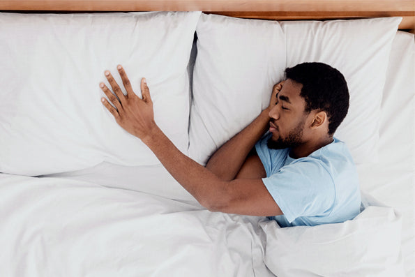 Image of a man asleep in bed with his head on the right pillow and his hand outstretched onto the left pillow