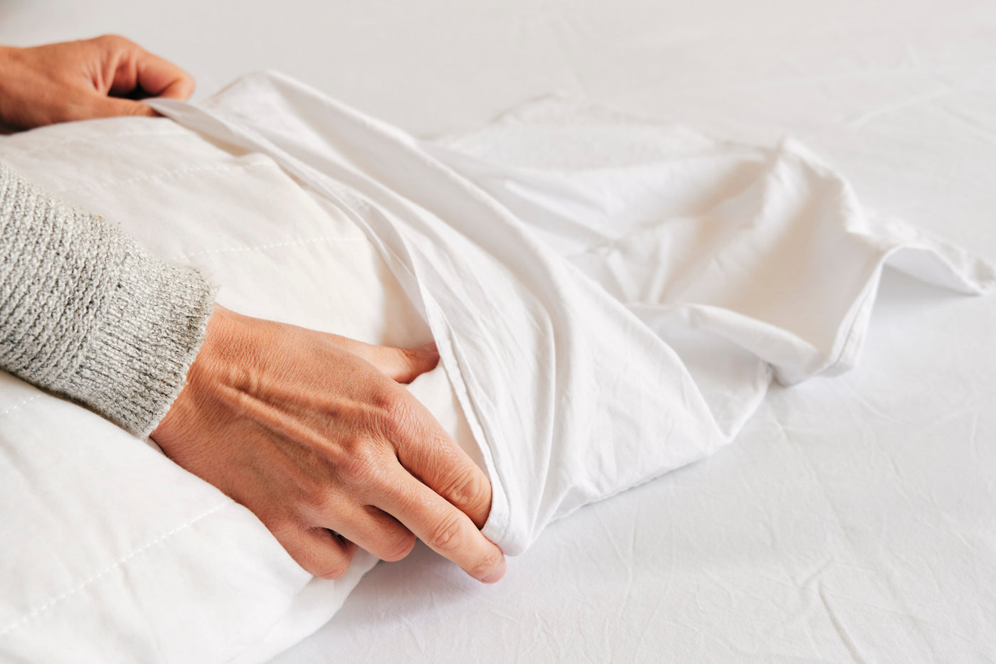 Image of a person's hands sliding a pillow into a white pillowcase on top of white sheets