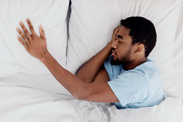 Image of a man asleep in bed with his head on the right pillow and his hand outstretched onto the left pillow