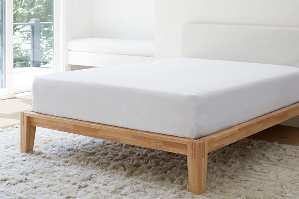 Image of a white bed with a mattress protector in a mostly white room