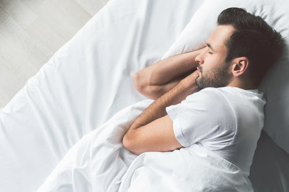 Image of a man asleep in bed on white sheets