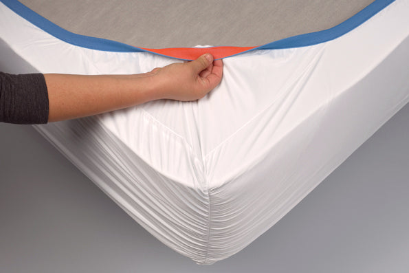Image of the Cooling or Warming Mattress Protector on the bottom side of a mattress showcasing the reversible elastic band with the blue side facing up and a hand twisting over a small portion of the orange side
